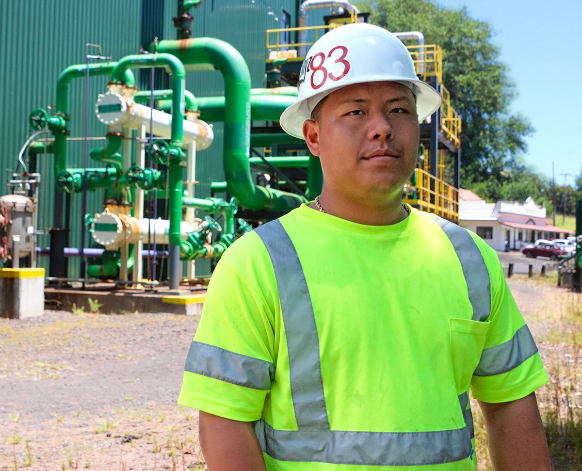 Honua Ola Employee in a yellow hi-viz reflective shirt, standing outside. He wears a hardhat and smiles at the camera.
